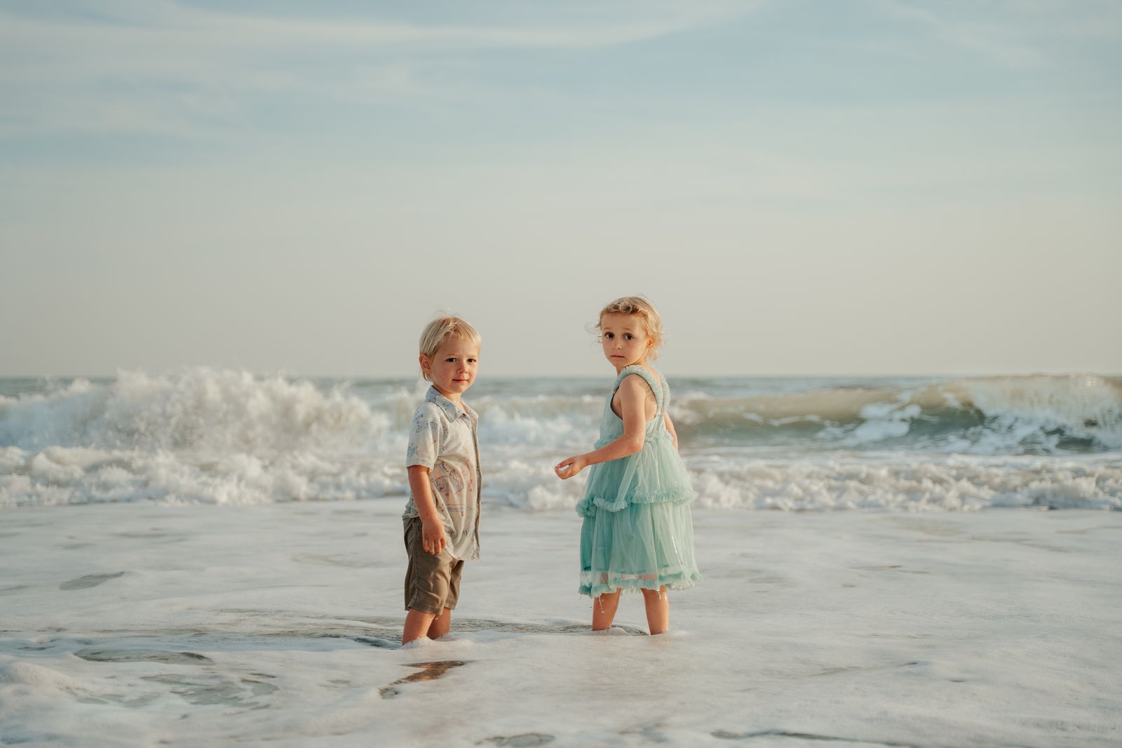 Two young siblings standing together in the ocean surf at the beach