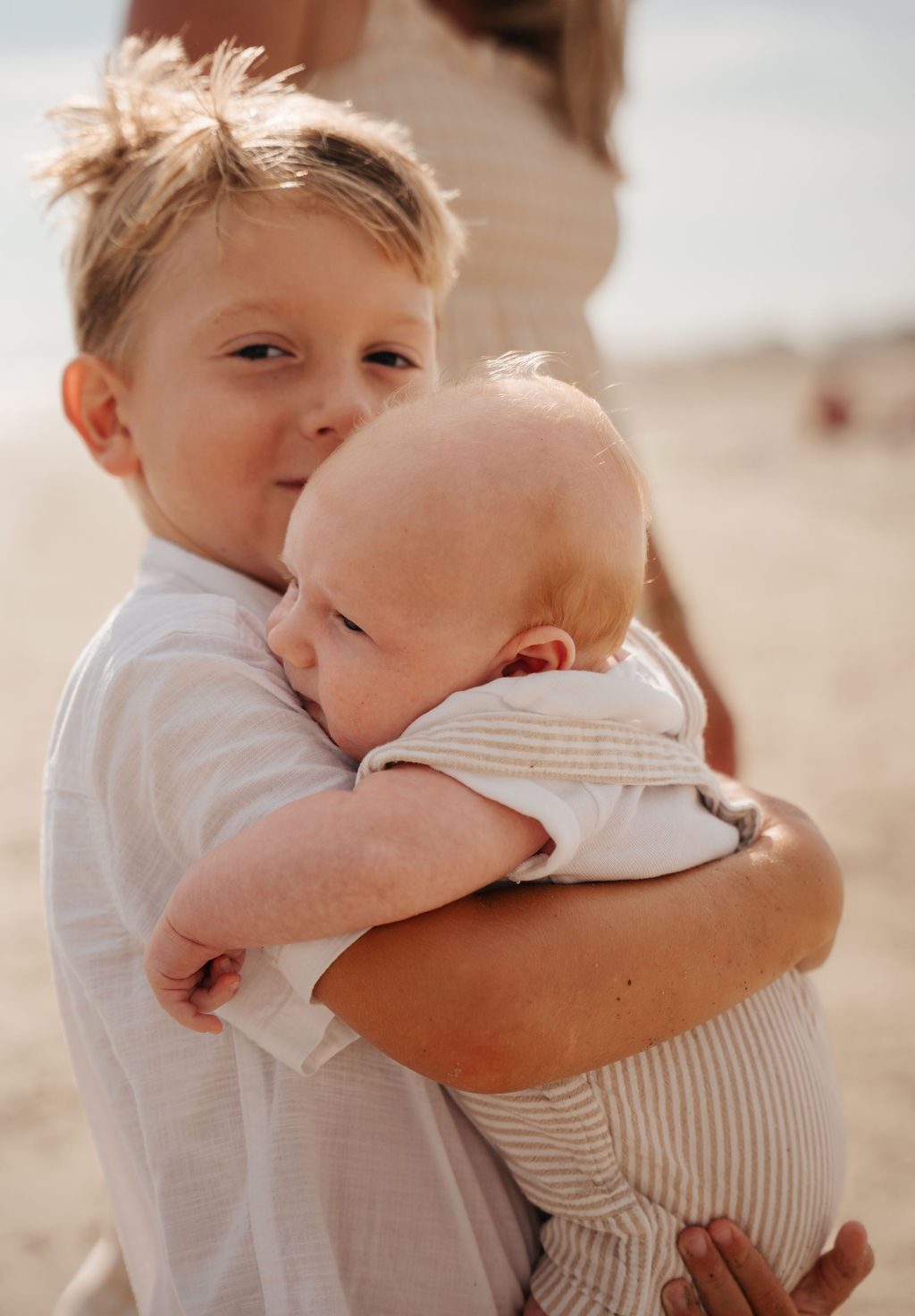Big brother holding his baby sibling close on the beach