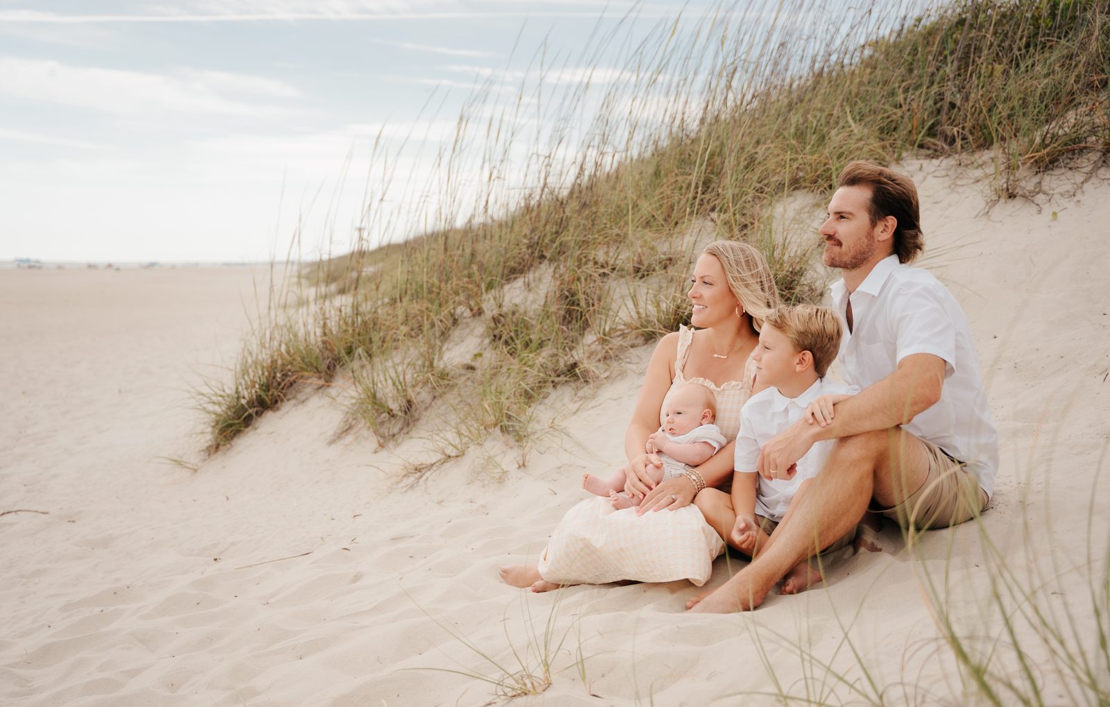 Family of four sitting together on a dune, looking out over the beach