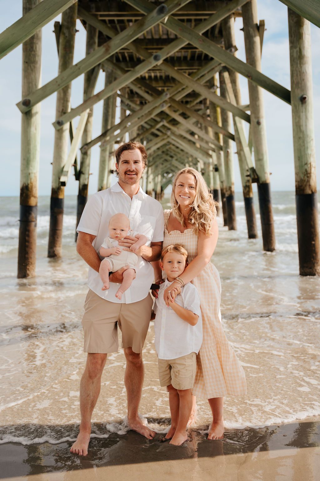 Family of four standing together beneath the pier pilings