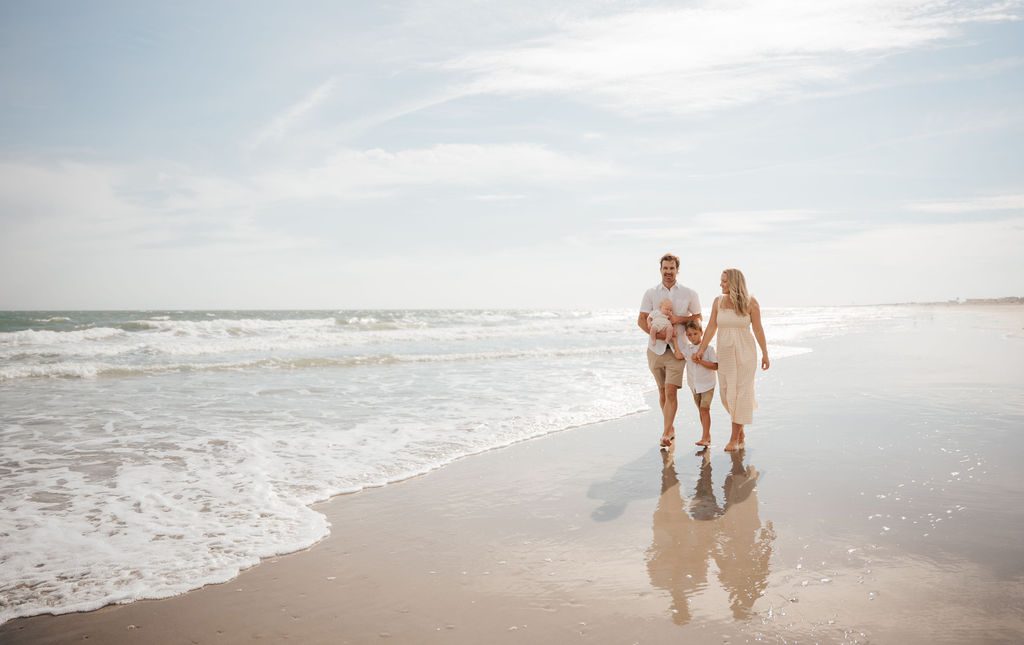 Family of four walking hand in hand along the shoreline