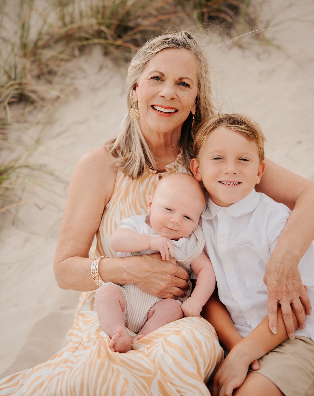Grandmother holding a baby with her grandson leaning in on the sand