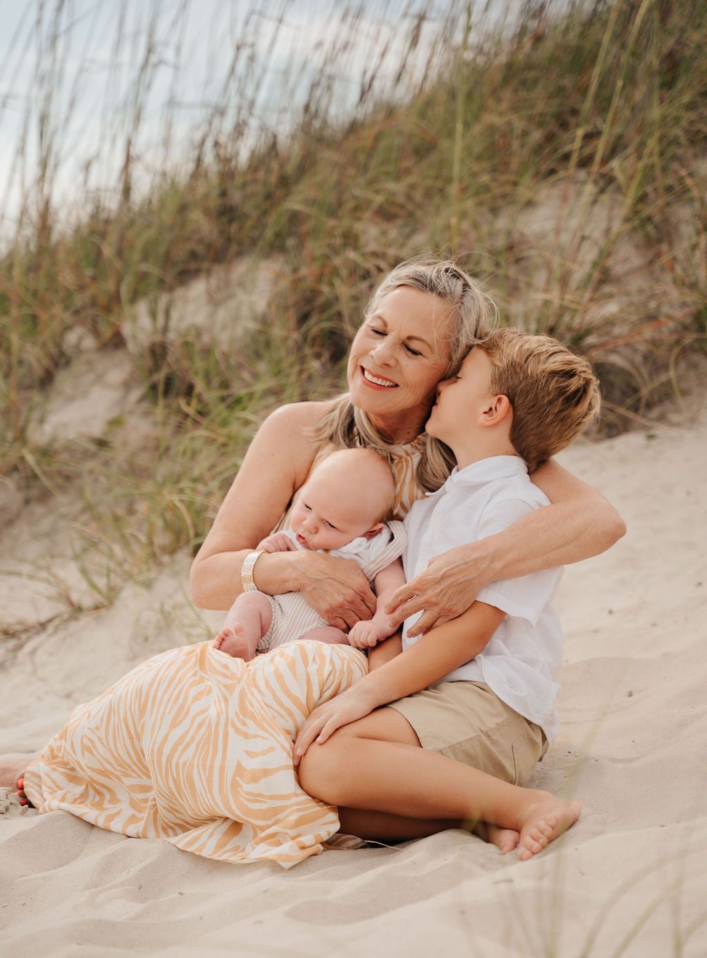 Grandmother kissing her grandson while holding the baby on the dune