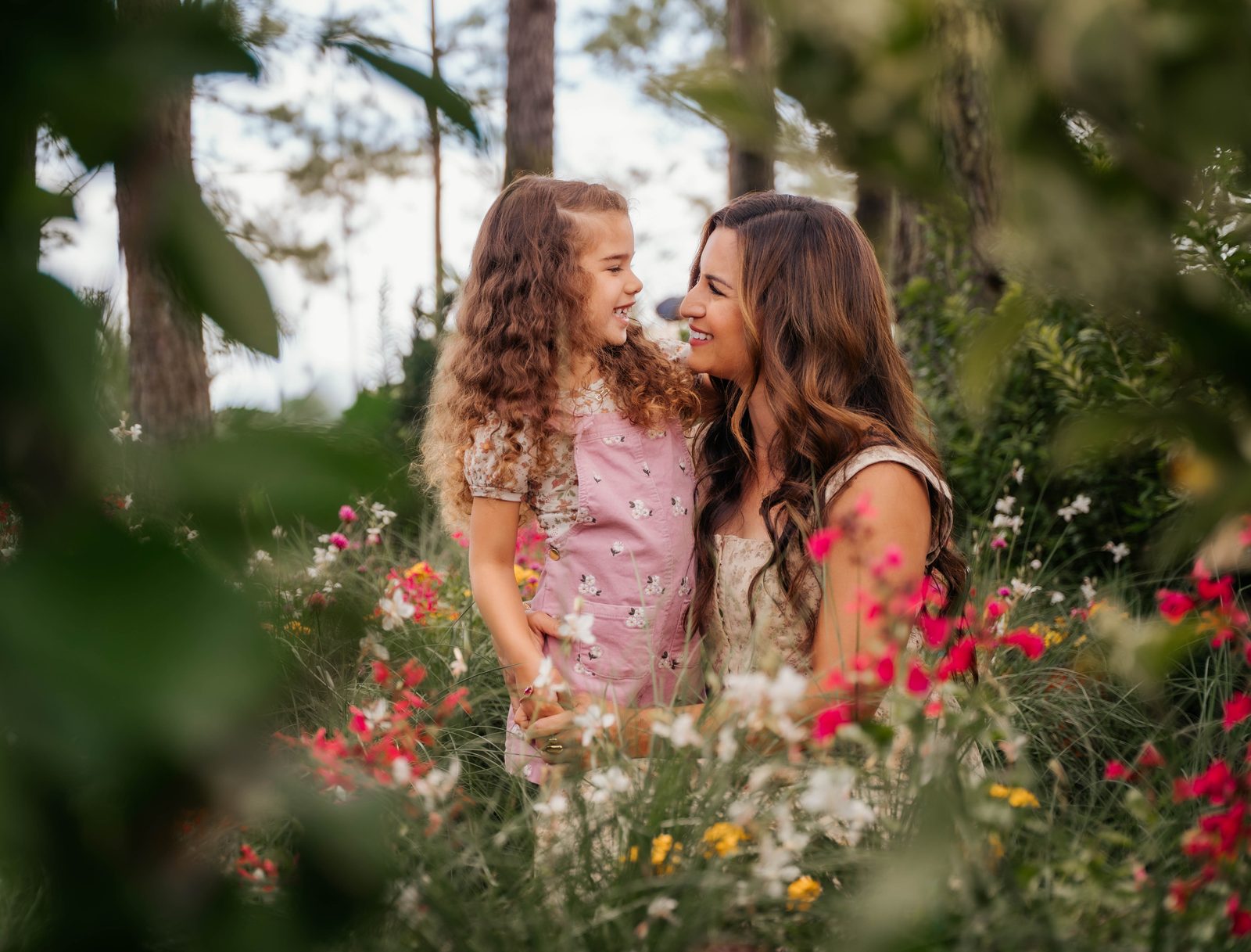 Mother and her curly haired daughter laughing face to face among the wildflowers