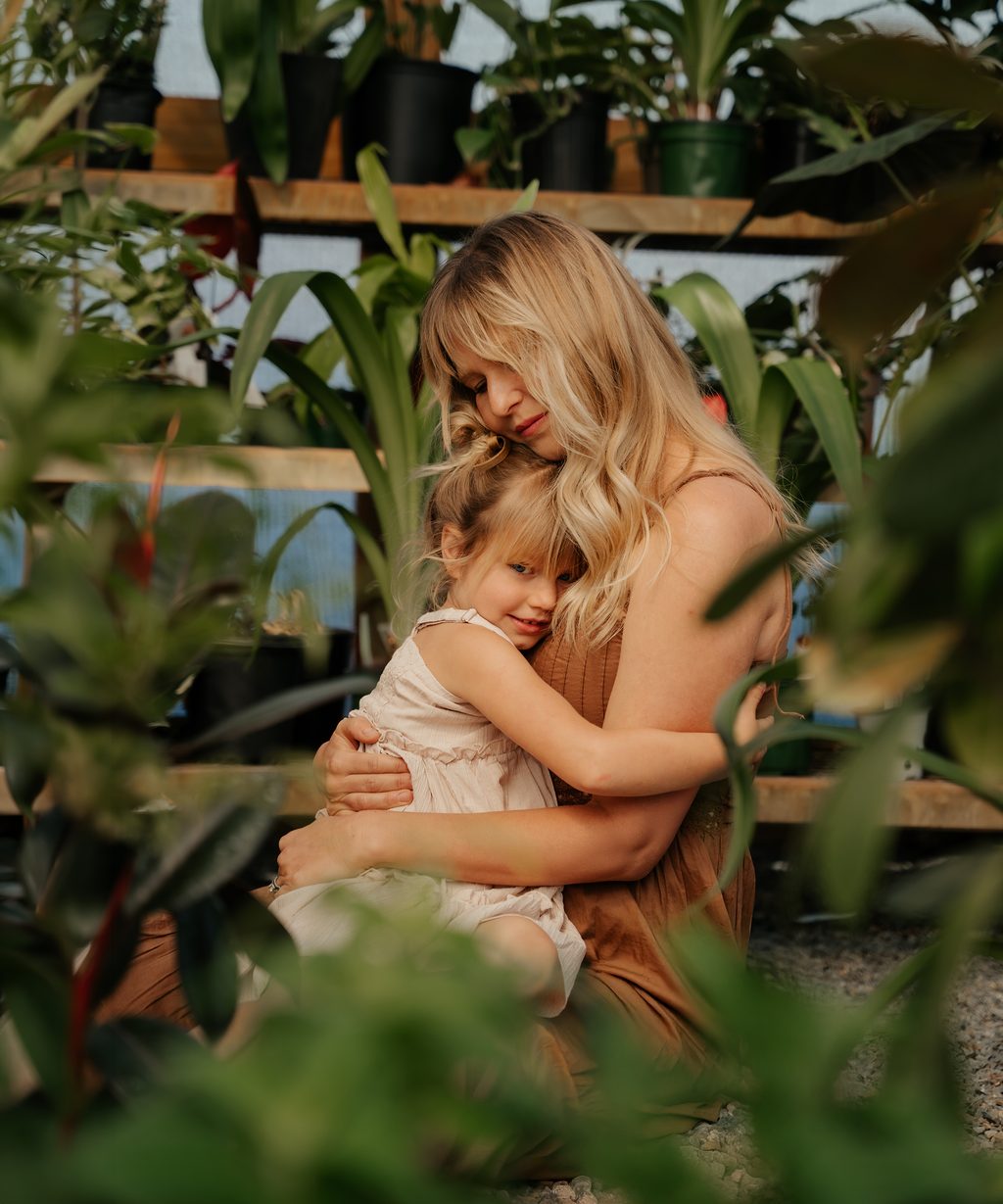 Mother kneeling to hug her daughter surrounded by greenhouse leaves