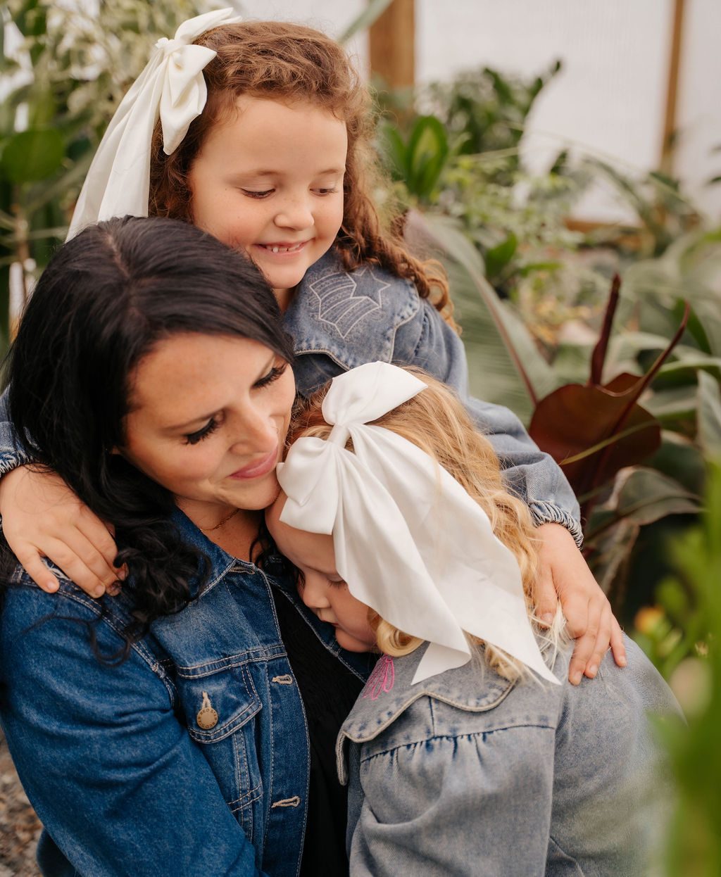Mother hugging both of her daughters in a greenhouse
