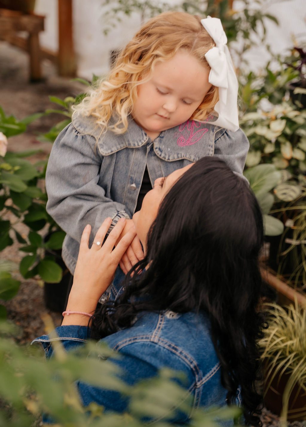 Mother lifting her blonde daughter up into her arms among the plants