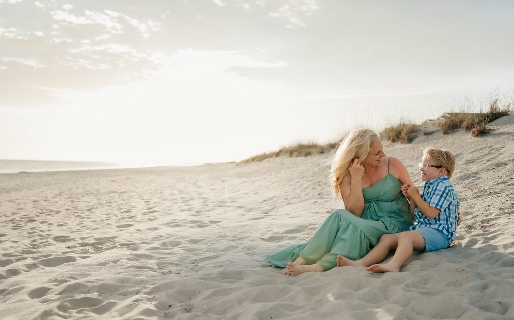 Mother in a green dress sitting on the sand laughing with her son