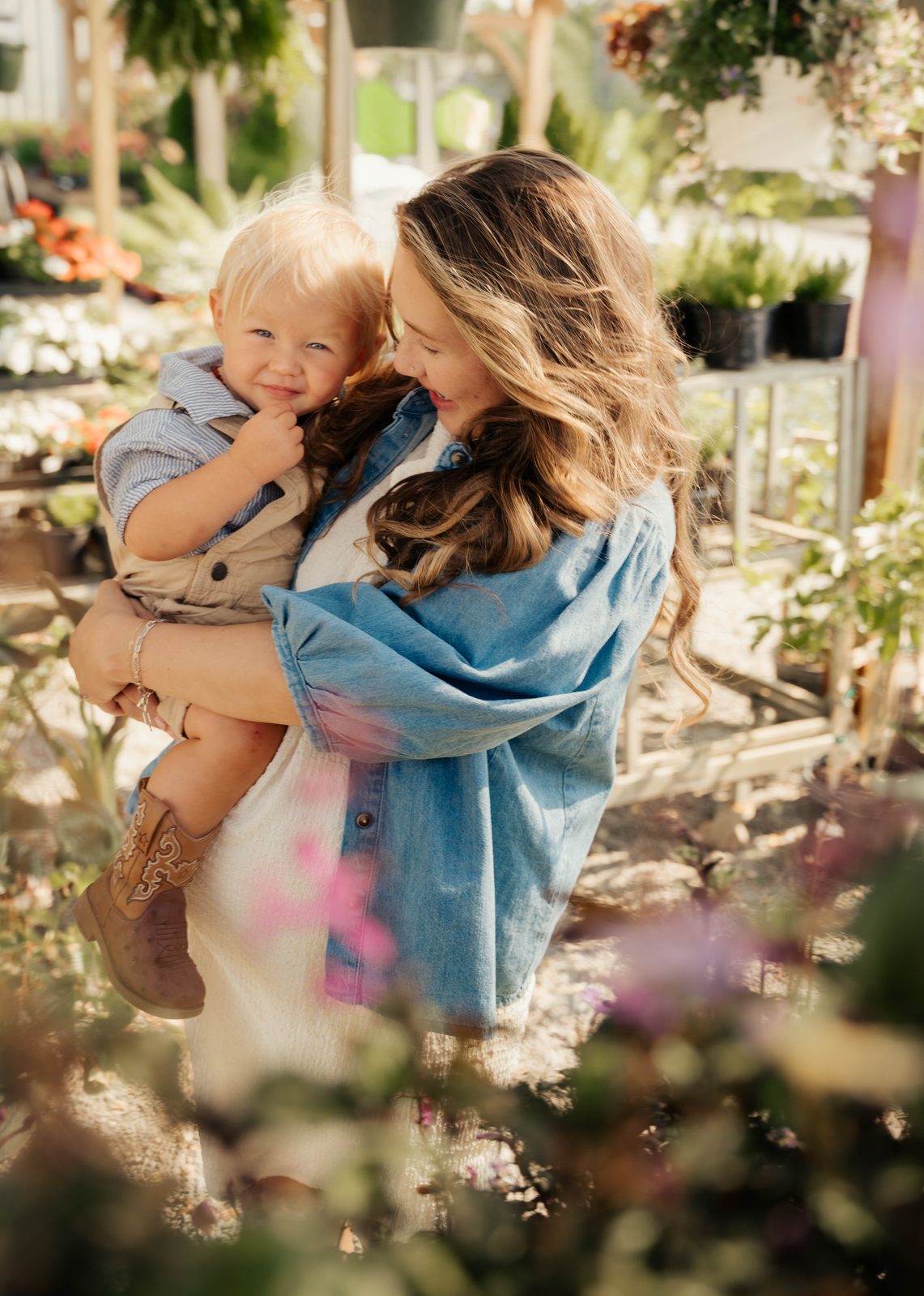 Mother carrying her toddler through a garden centre in warm afternoon light