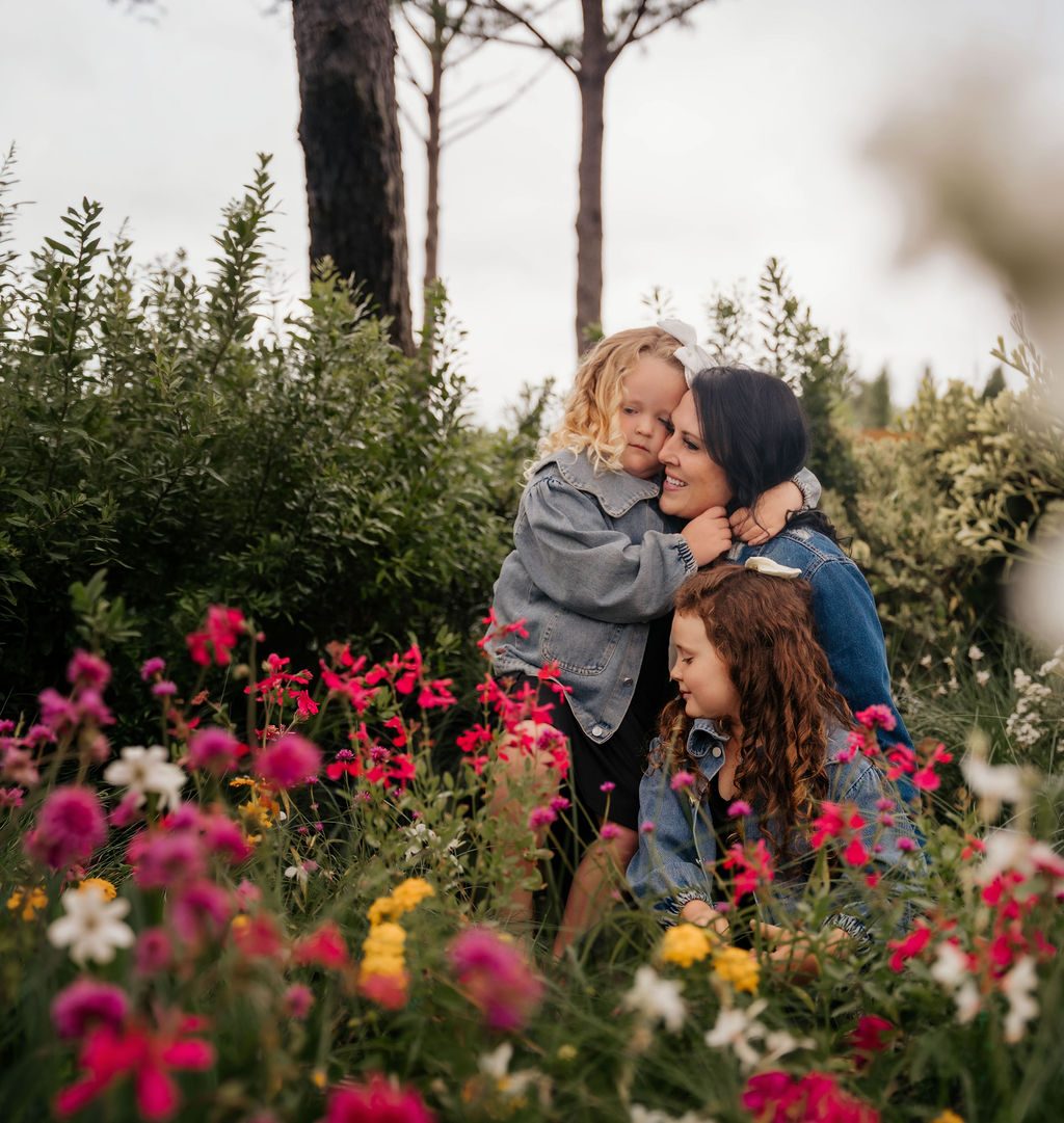 Mother holding her two daughters among tall pink and white wildflowers