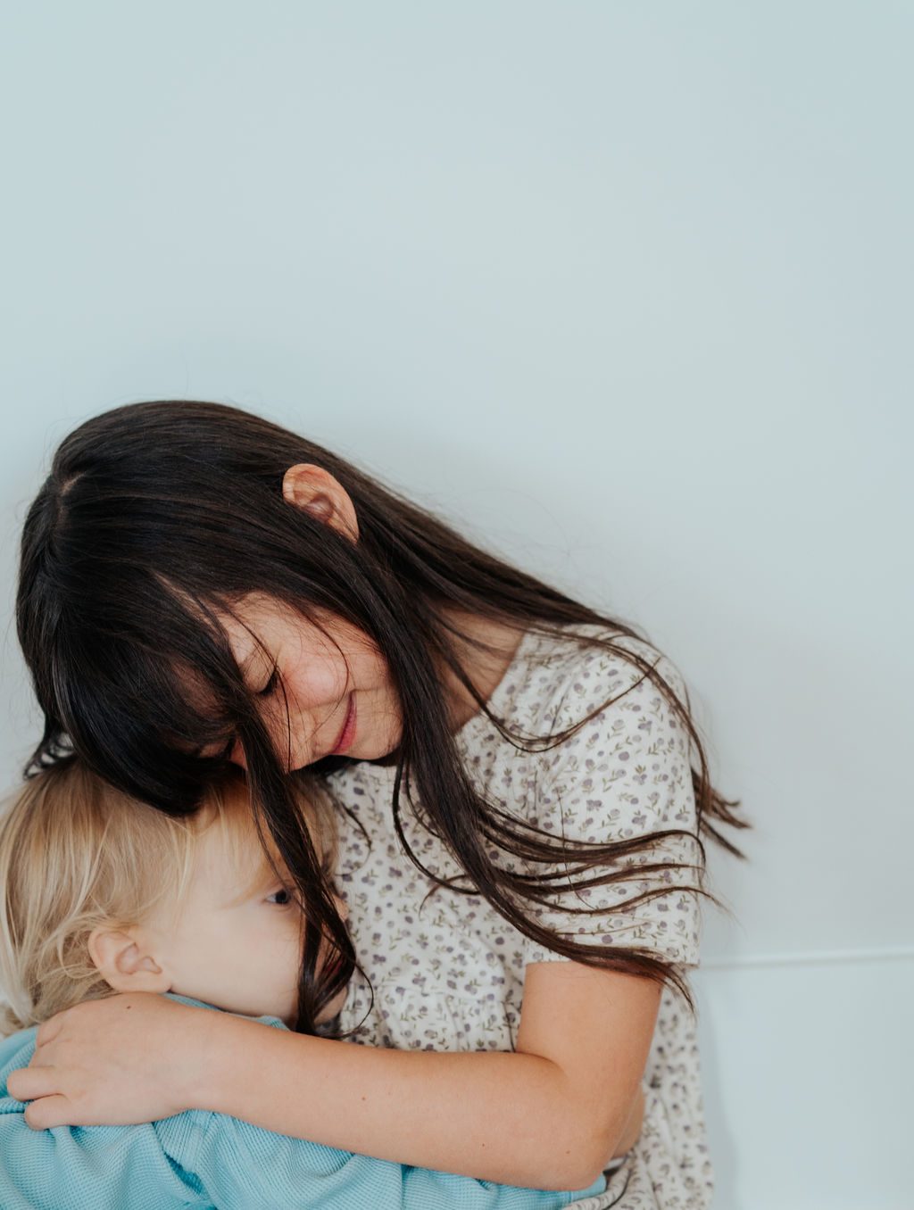 Big sister wrapping her arms around her little brother against a pale wall