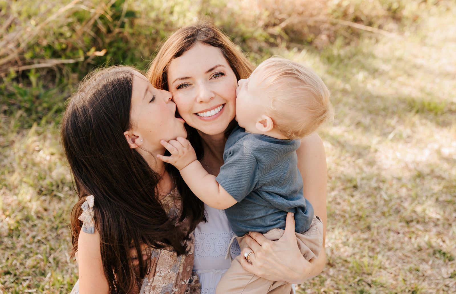 Erica with her two kids kissing her cheeks in a golden outdoor setting