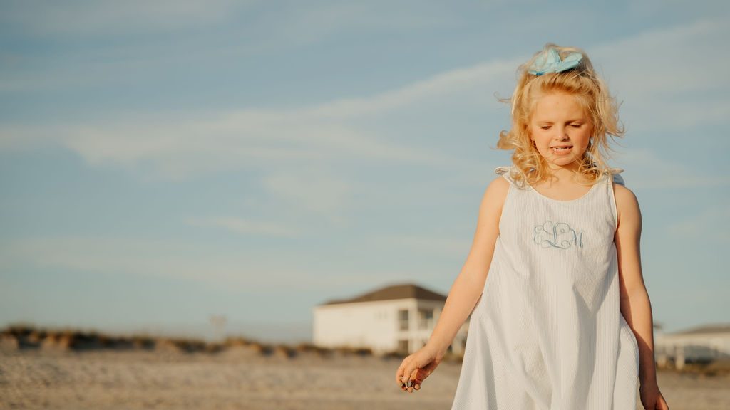Young girl in a white dress walking on the beach at sunset