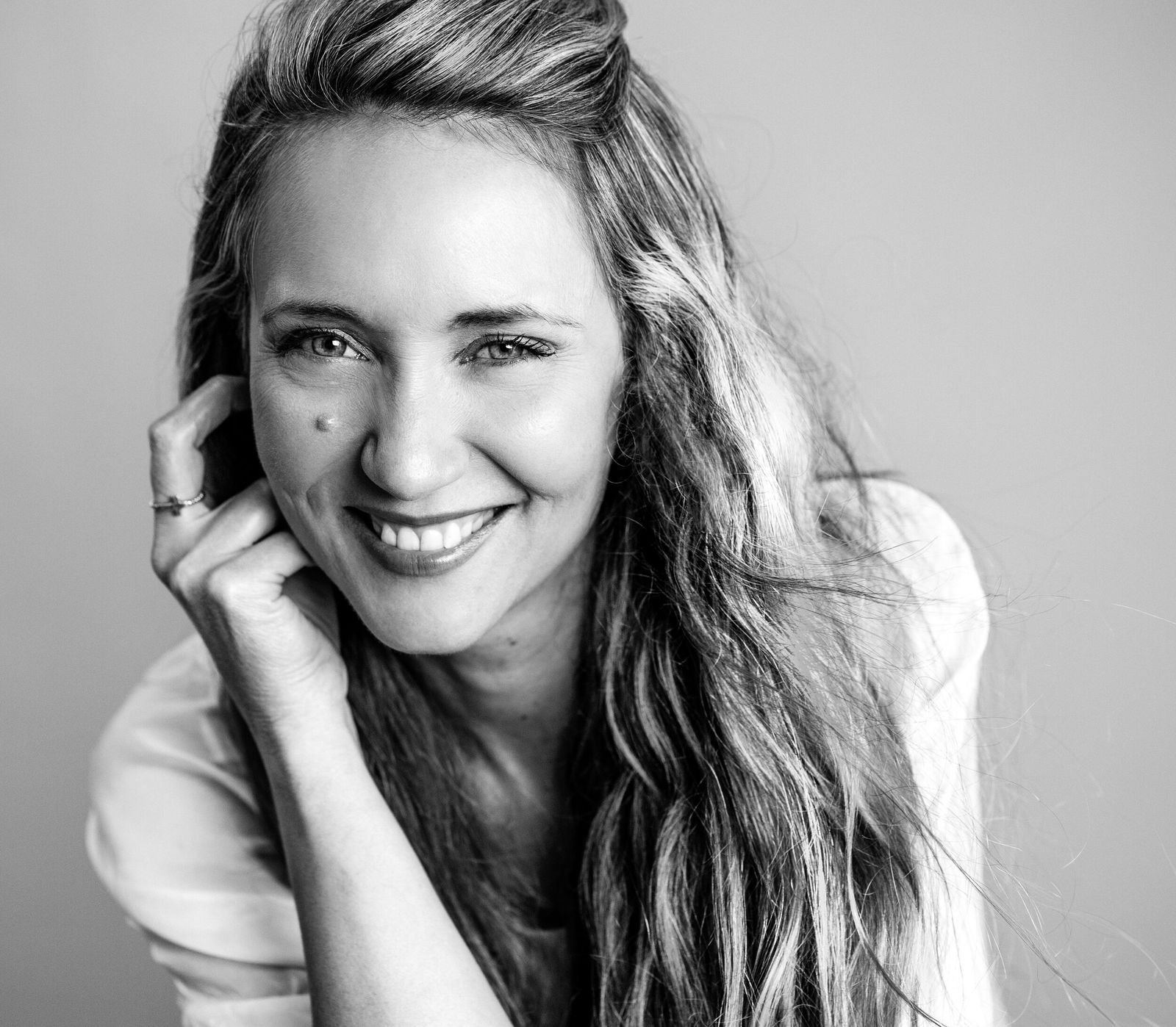 Black and white portrait of a woman smiling with her hand resting near her chin