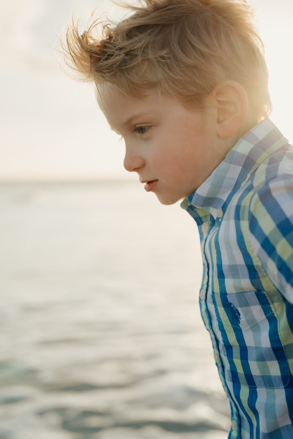 Boy in a blue plaid shirt looking down at the water
