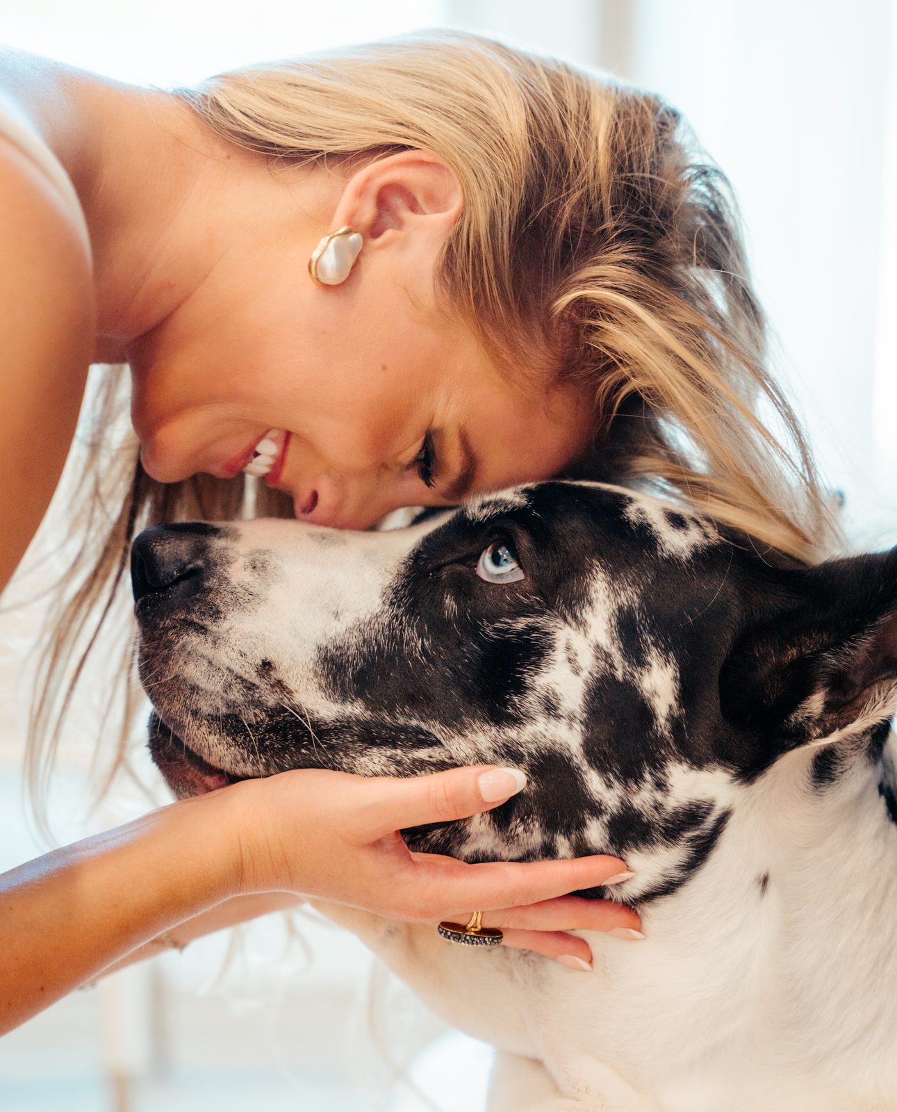 Woman resting her forehead against the head of a black and white Great Dane