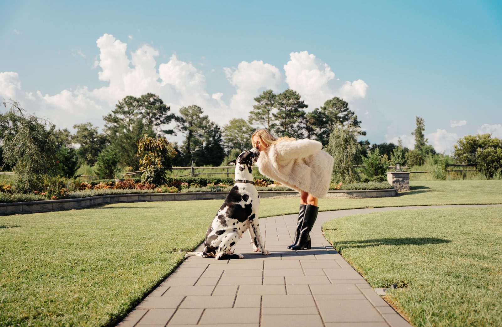 Woman leaning down to kiss her Great Dane on a garden path