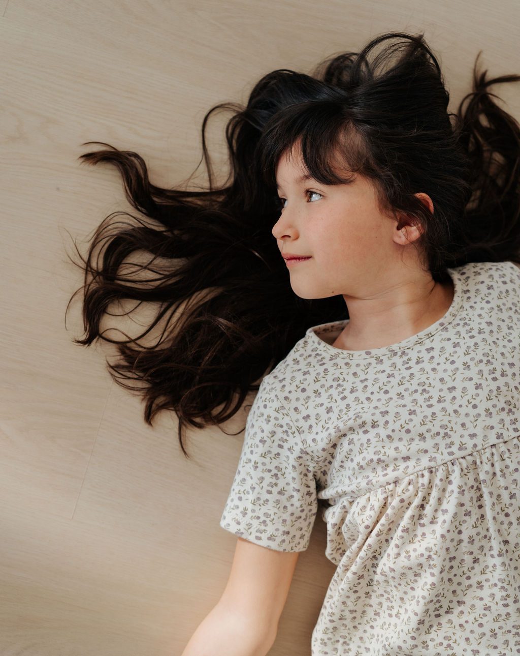 Girl lying on a pale floor with her dark hair fanned out around her