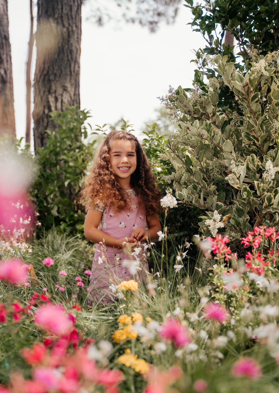 Girl in pink floral overalls standing in a garden of tall wildflowers