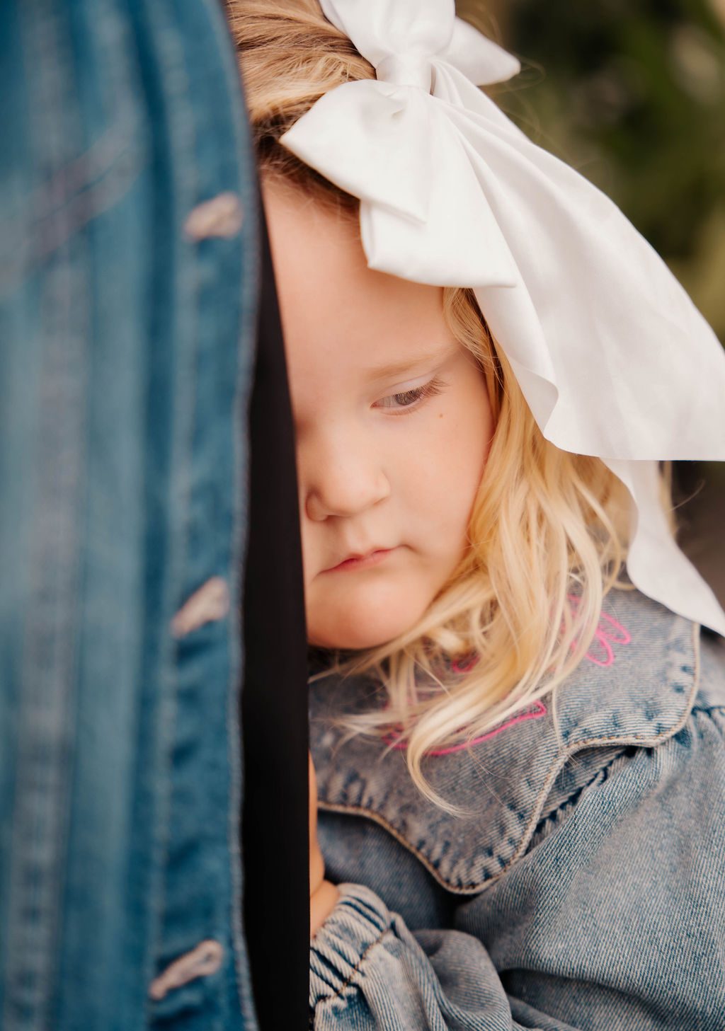 Close portrait of a girl with a white bow resting against a denim jacket