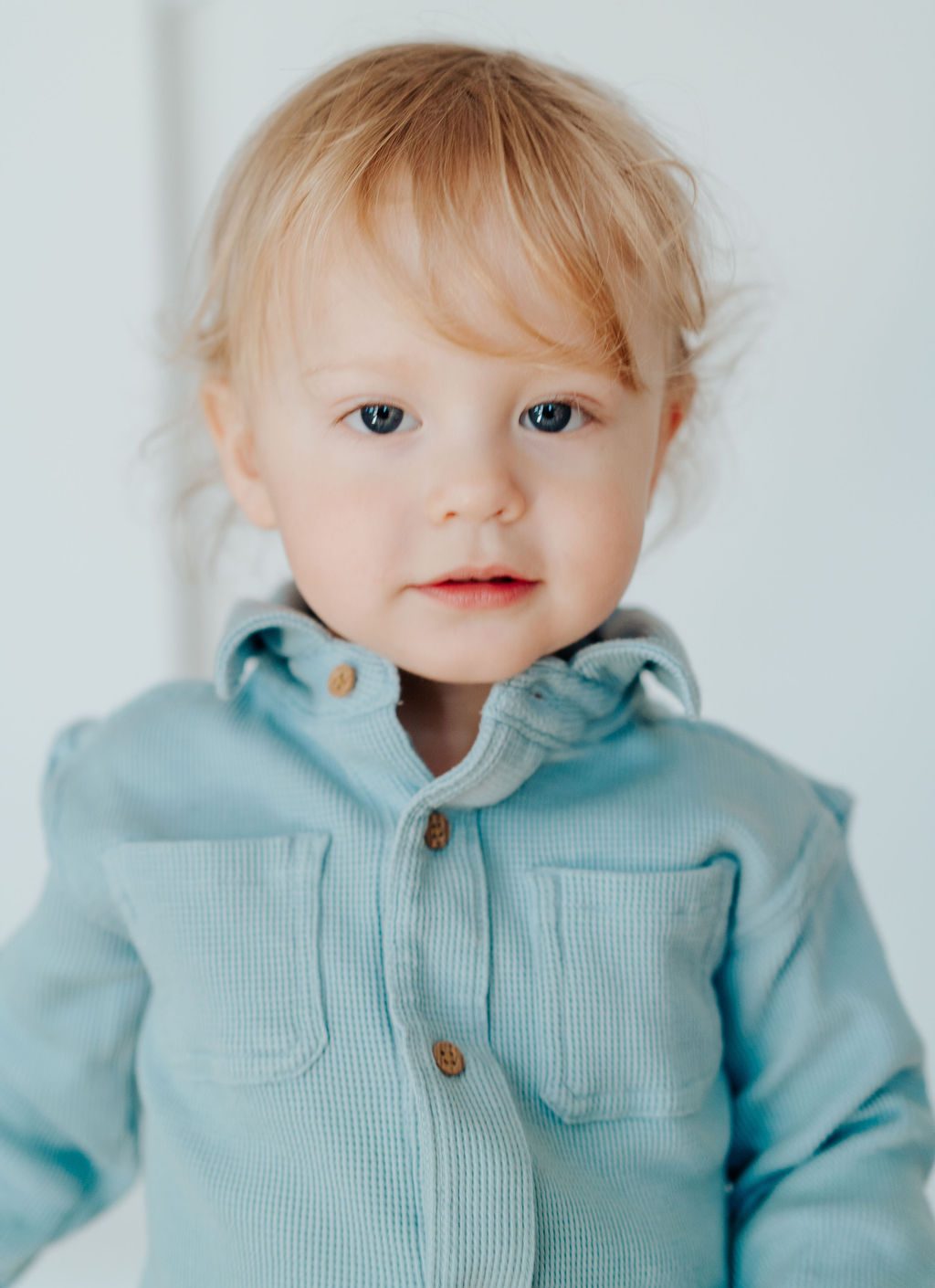 Close portrait of a blonde toddler in blue looking at the camera