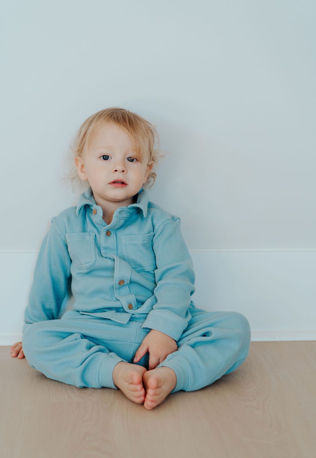 Toddler in a blue waffle outfit sitting against a pale wall