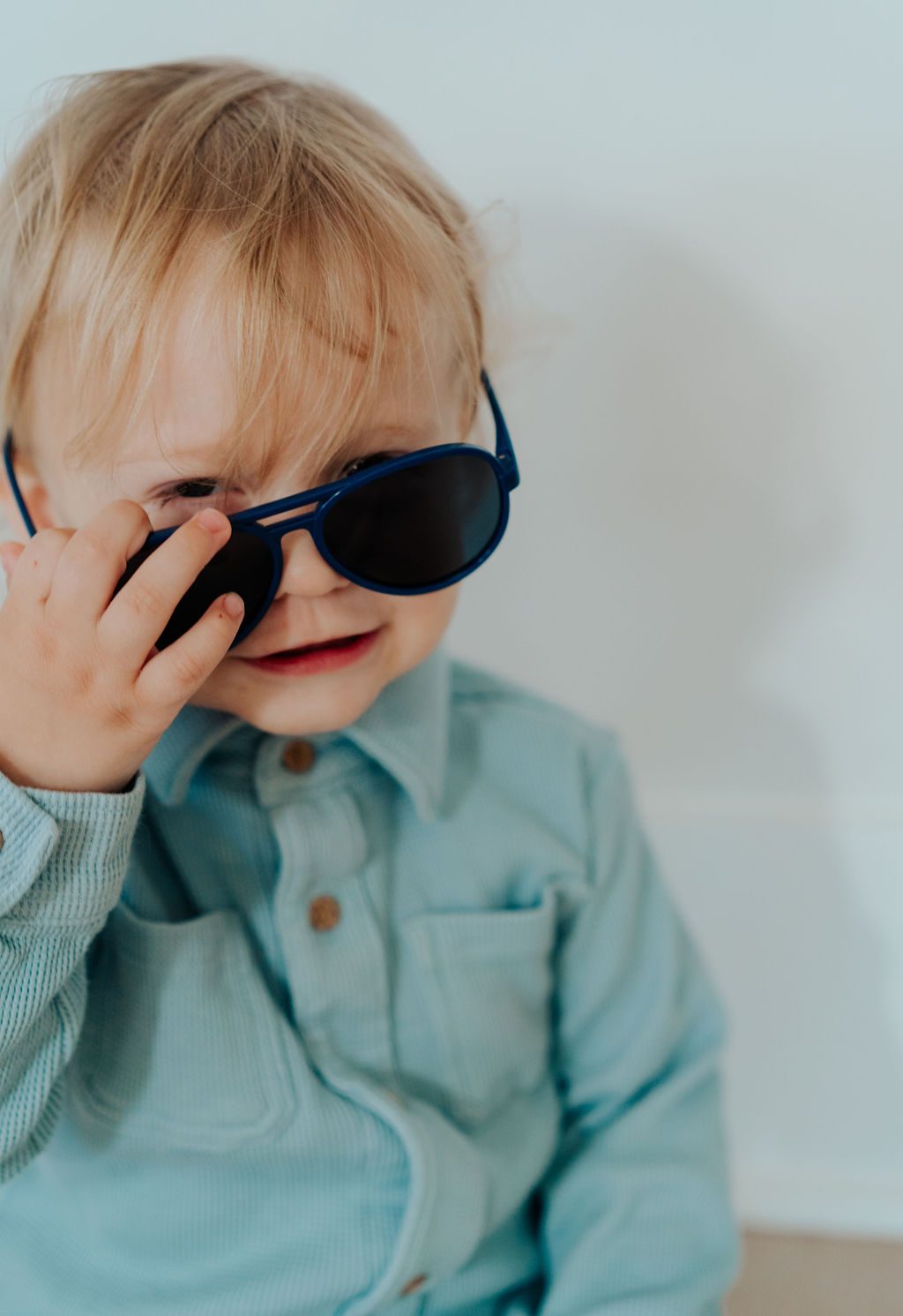 Toddler peeking out from behind a pair of blue sunglasses