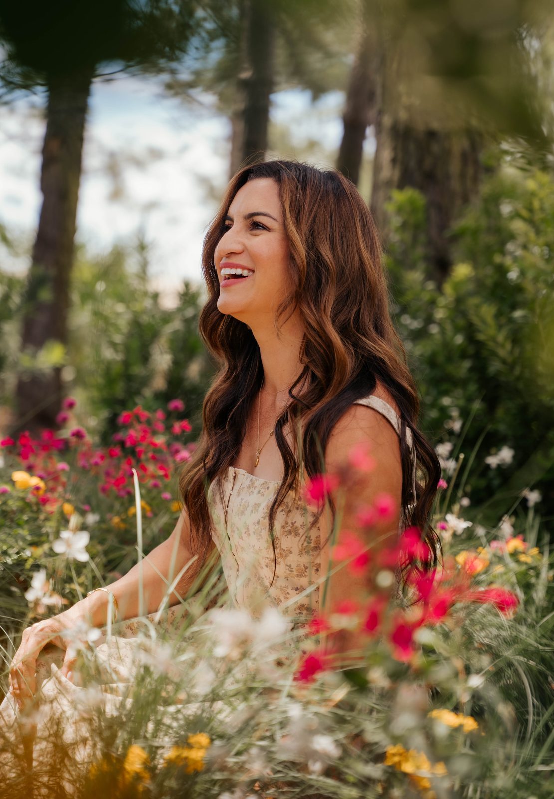 Woman laughing in profile, seated in a field of wildflowers in golden light