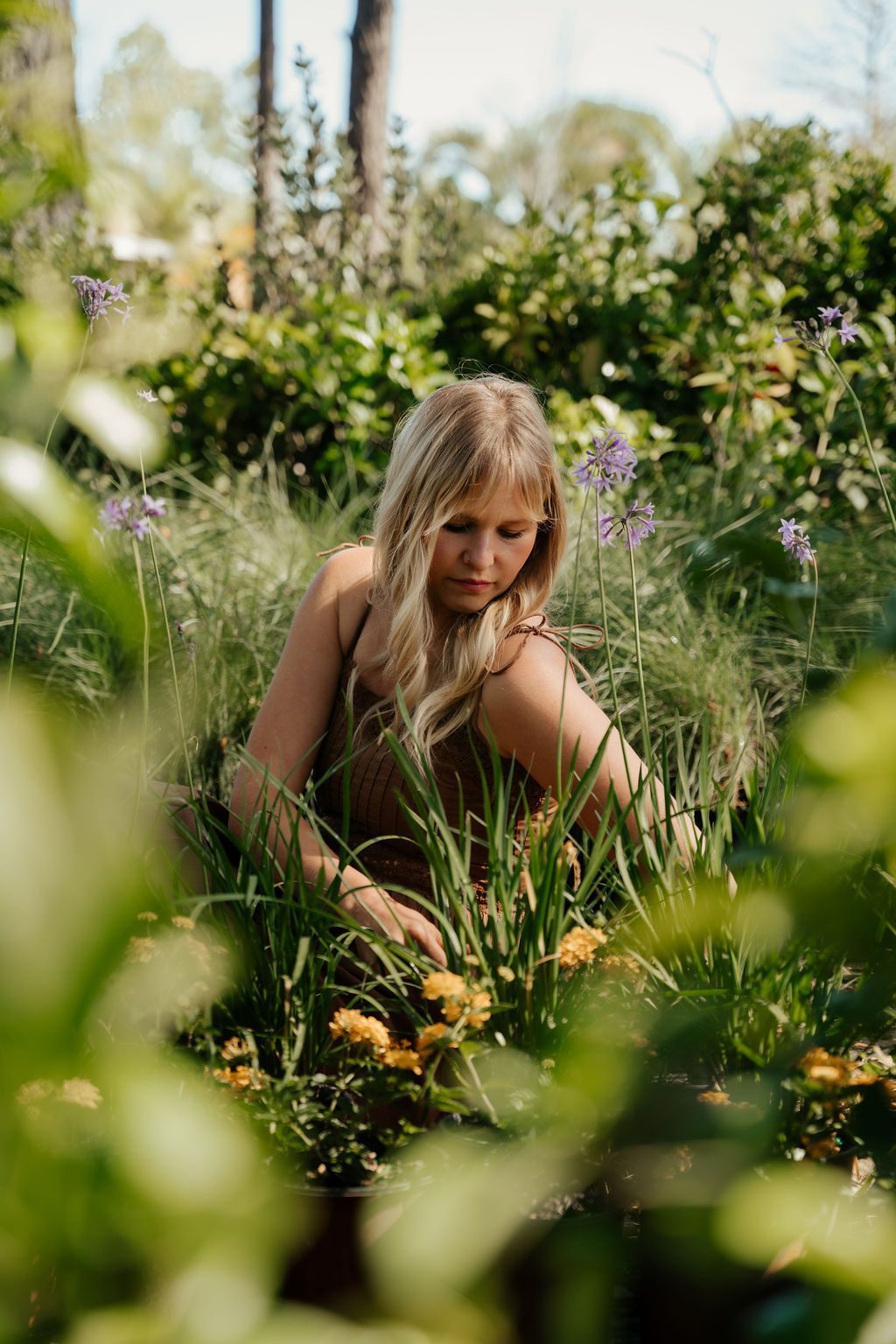 Woman in a brown dress crouching among the flowers in a nursery