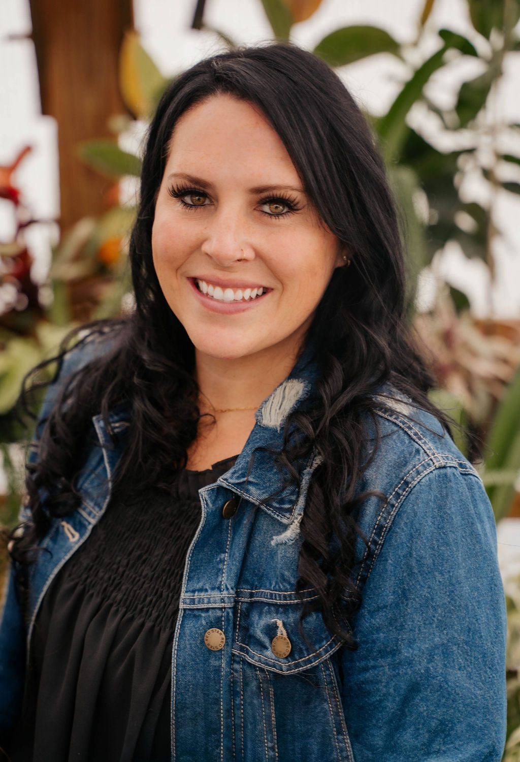 Portrait of a woman in a denim jacket smiling among greenhouse plants