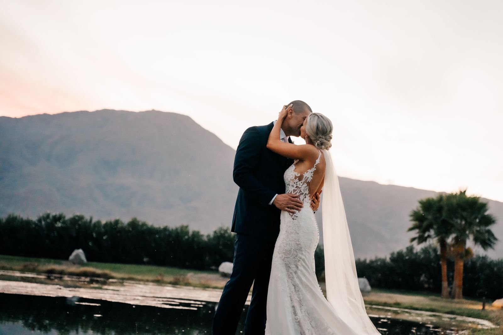 Bride and groom sharing a kiss at sunset with mountains and a lake in the background
